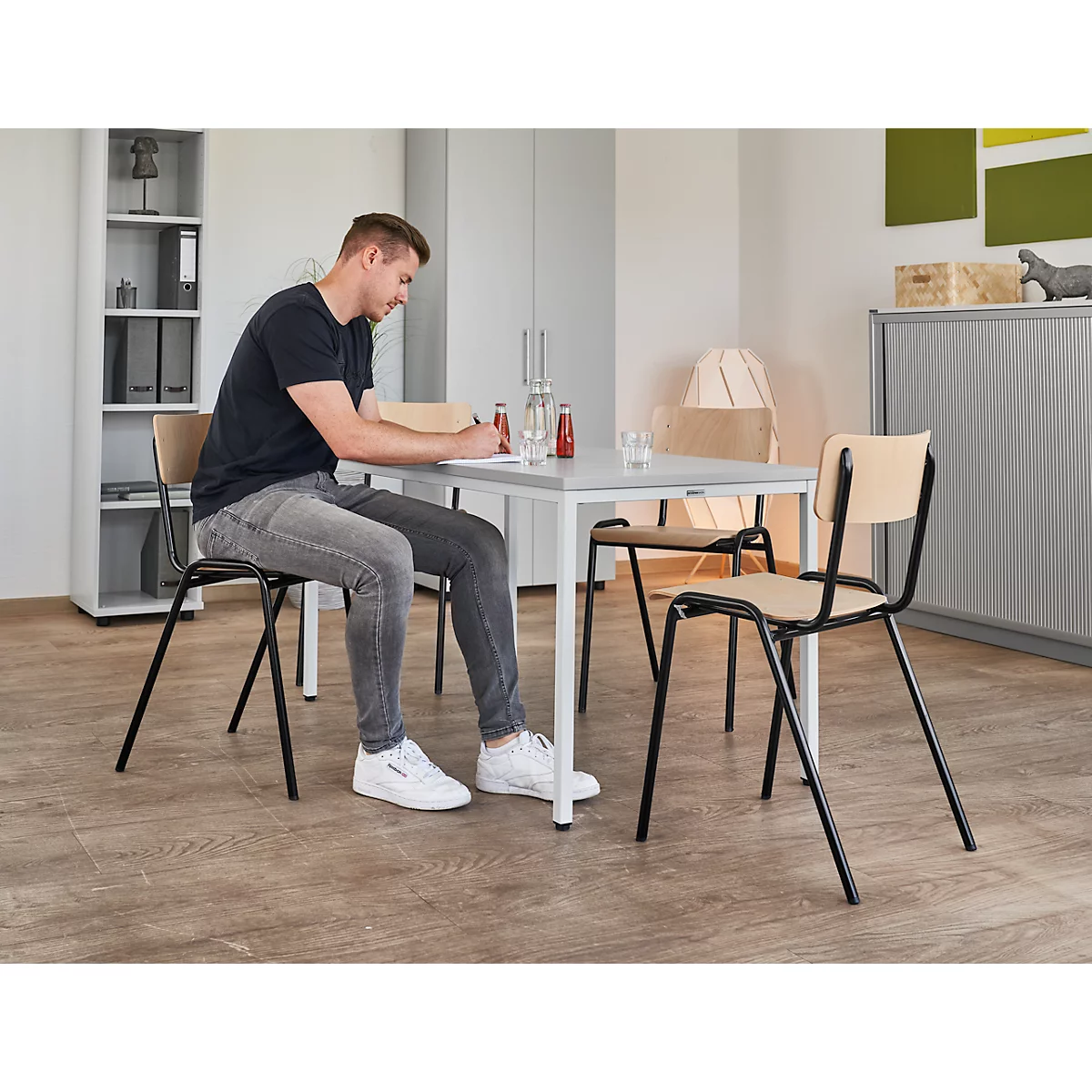 Man sits at a table writing. On the table are a bottle, a glass and a sauce bottle.