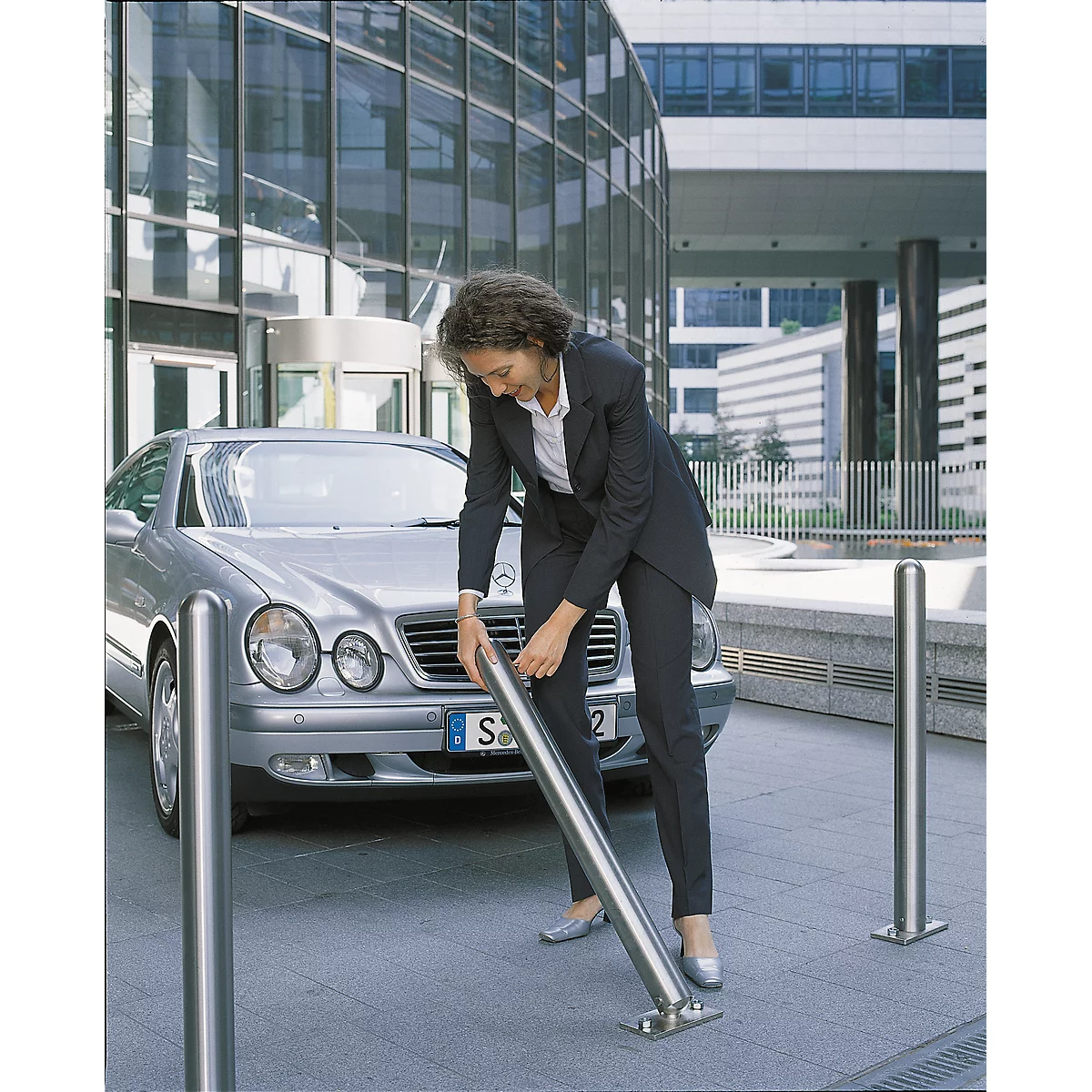 Business woman in suit installing a stainless steel bollard. A silver car is next to her.