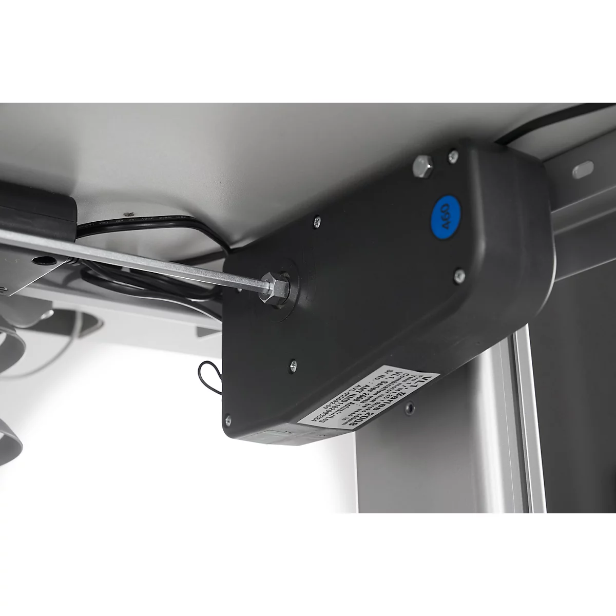 Gray motor under a table top, with cables, screws and a blue sticker.