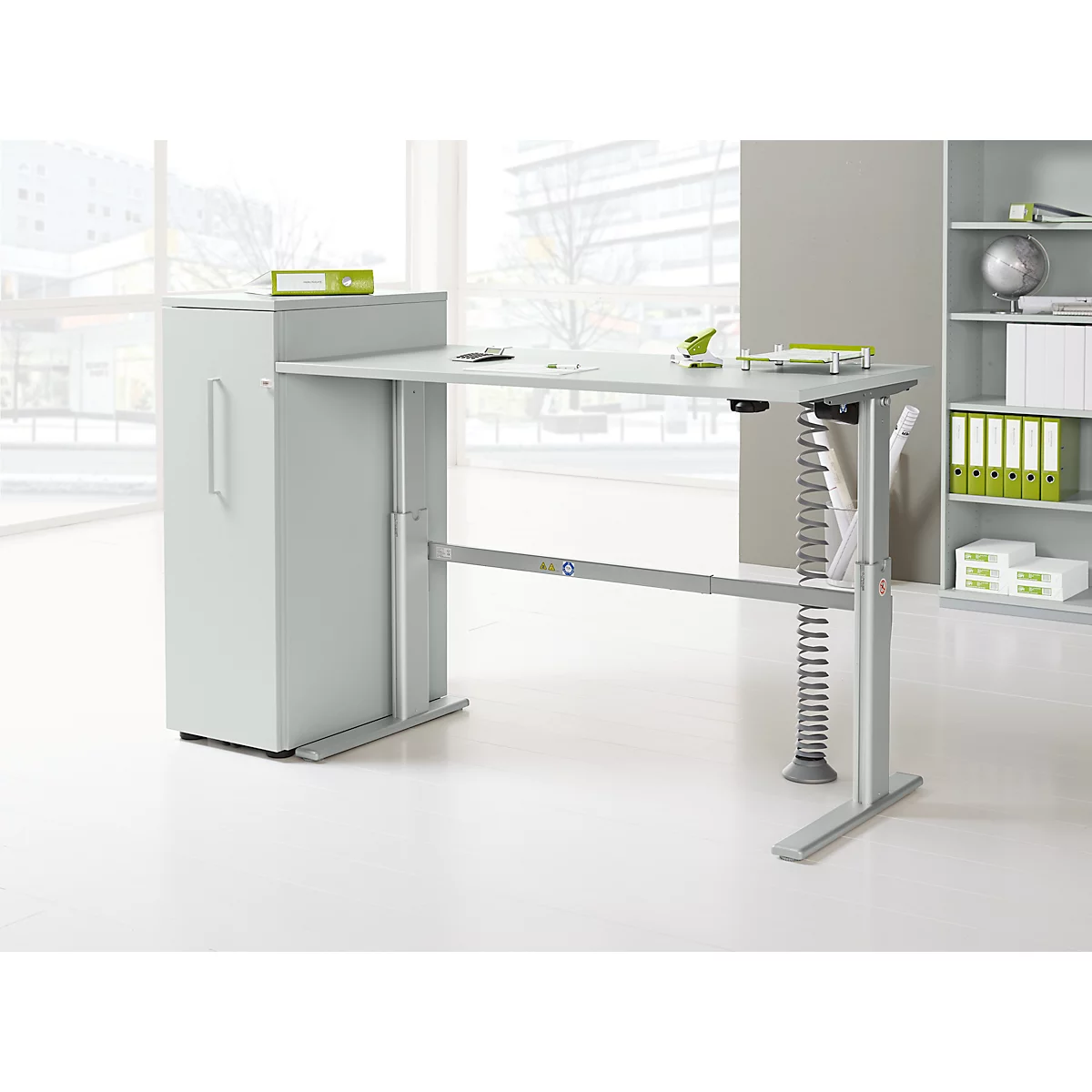 Light gray height-adjustable desk with integrated cabinet against a bright background.
