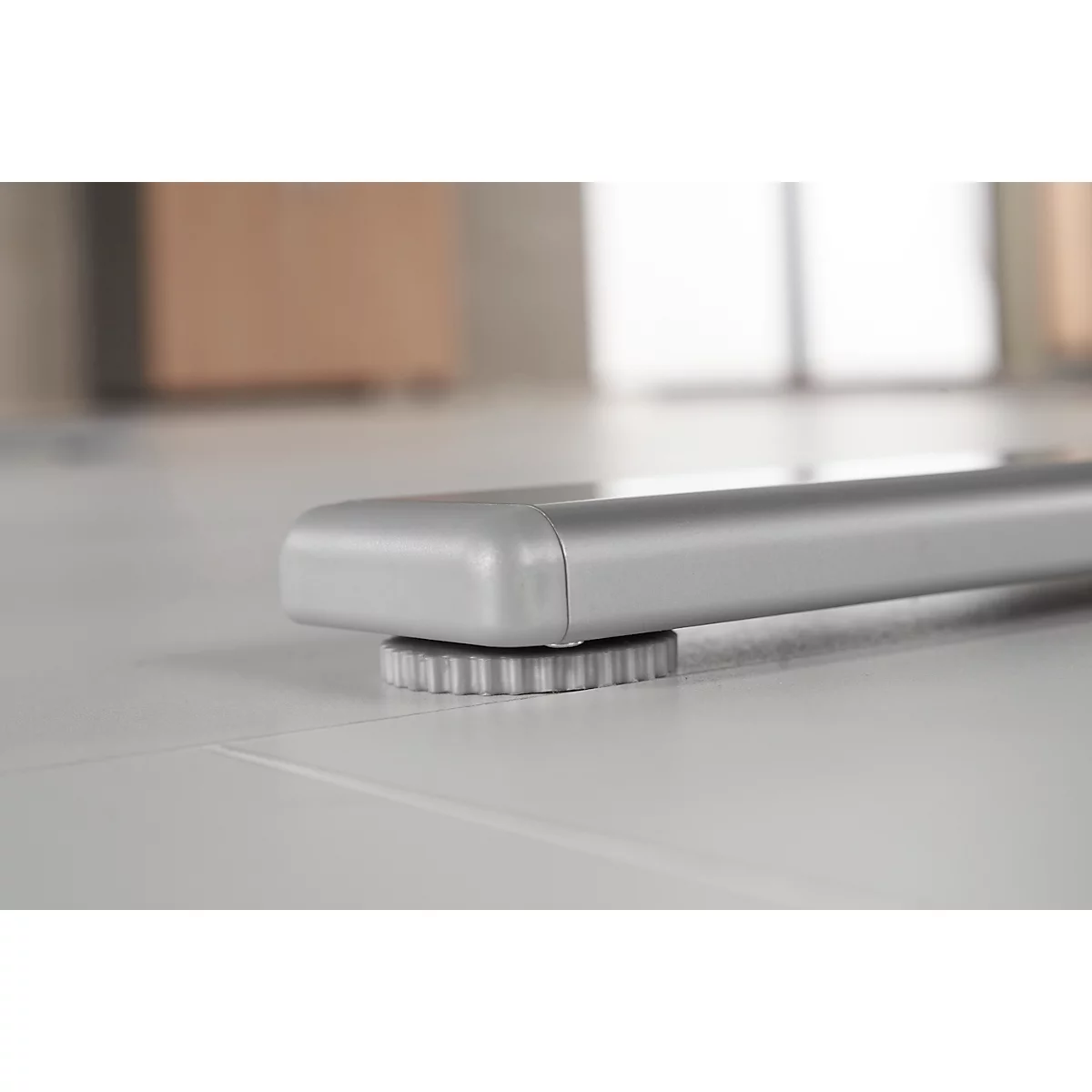 Close-up of a silver table leg construction. The table foot stands on a round, toothed plastic part.