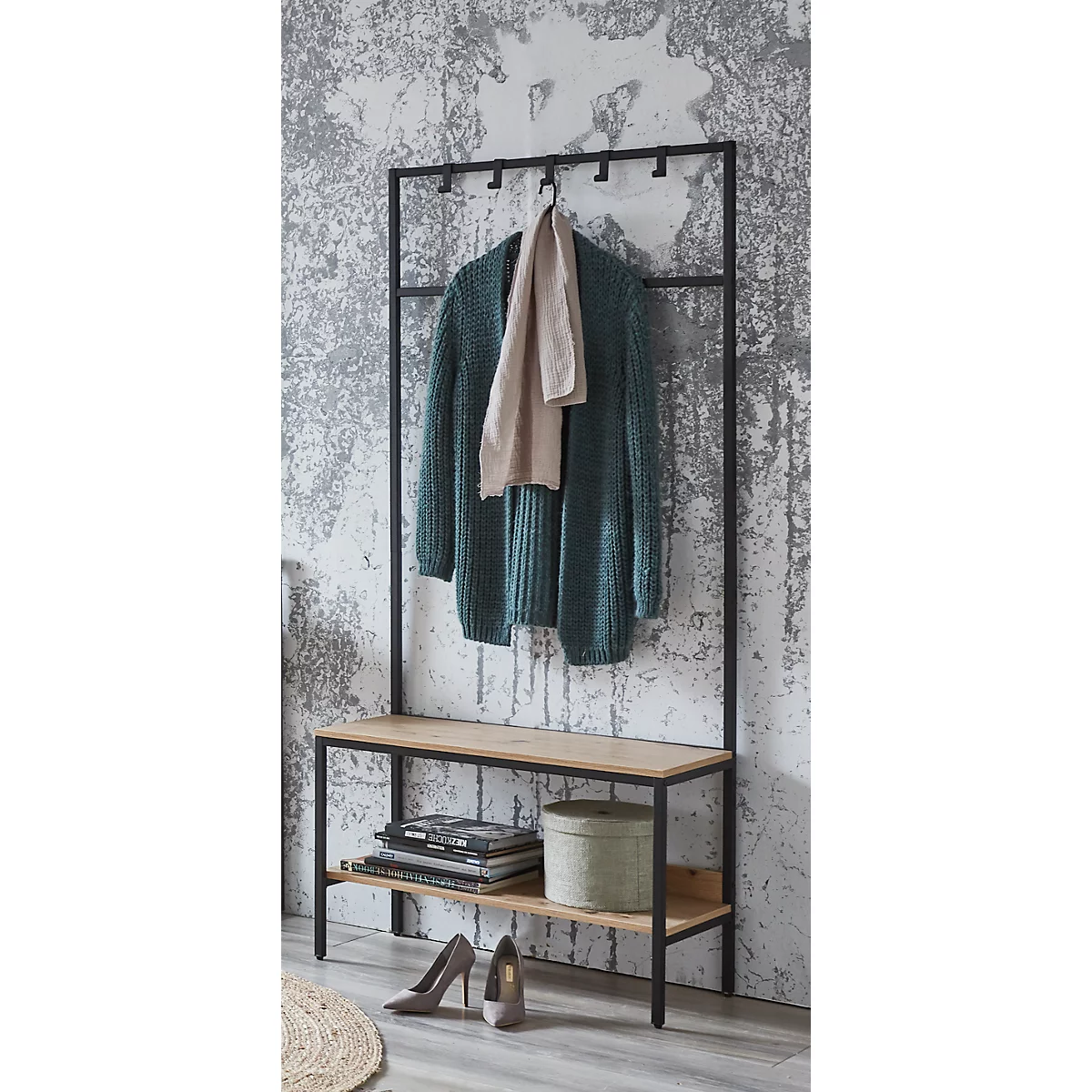 Schwarzer Kleiderständer mit grüner Strickjacke, hellem Schal und Bank. Darauf Schuhe, Zeitschriften, Dose.