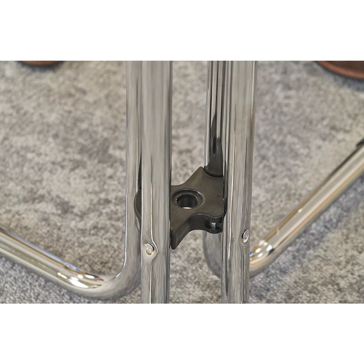 Close-up of a chair. Chrome legs connected by a black plastic element, on gray carpet.