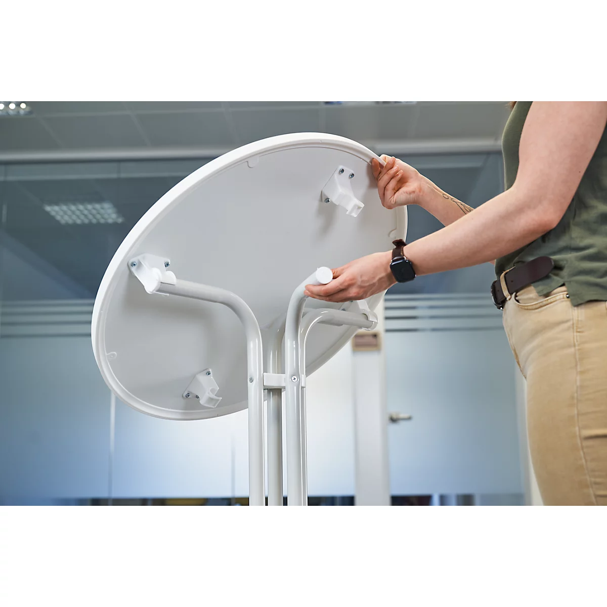 Person assembling a white table. Bright table top and table legs are visible.