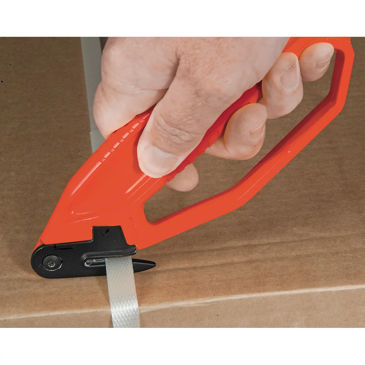 A hand holds a red strapping tool, tensioning a white strap on a cardboard box.