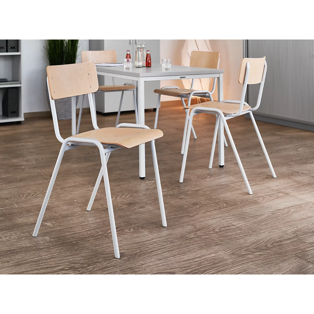 Verschillende witte stoelen met lichte houten zittingen en rugleuningen staan rond een tafel.