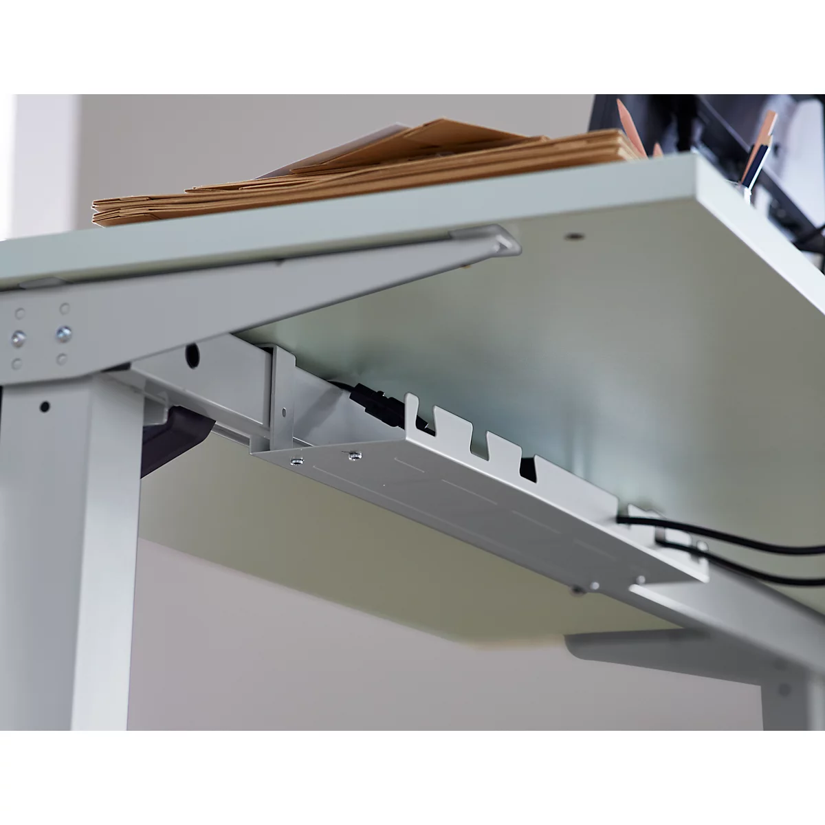 Close-up of the underside of a white desk with cable management. Cables and brackets held.