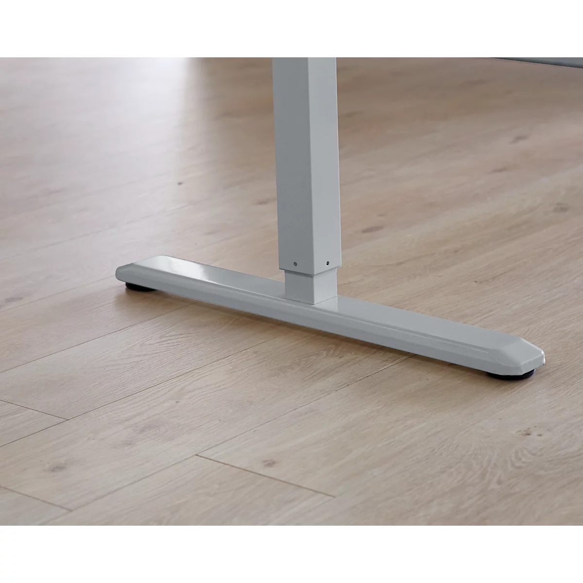 Close-up: Light gray desk foot with black rubber buffer on light wood floor.