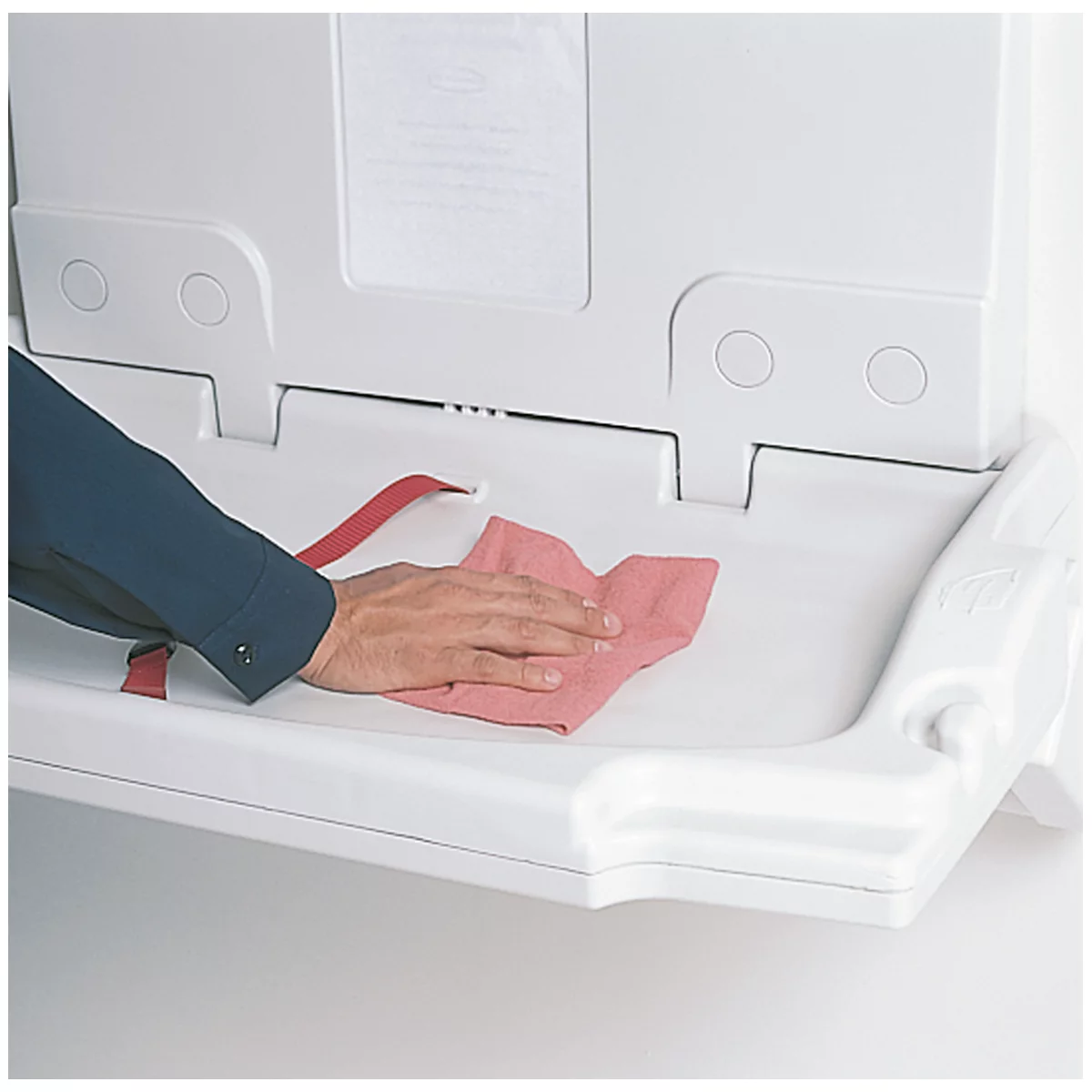 Une main nettoie une table à langer murale blanche avec un chiffon rouge.