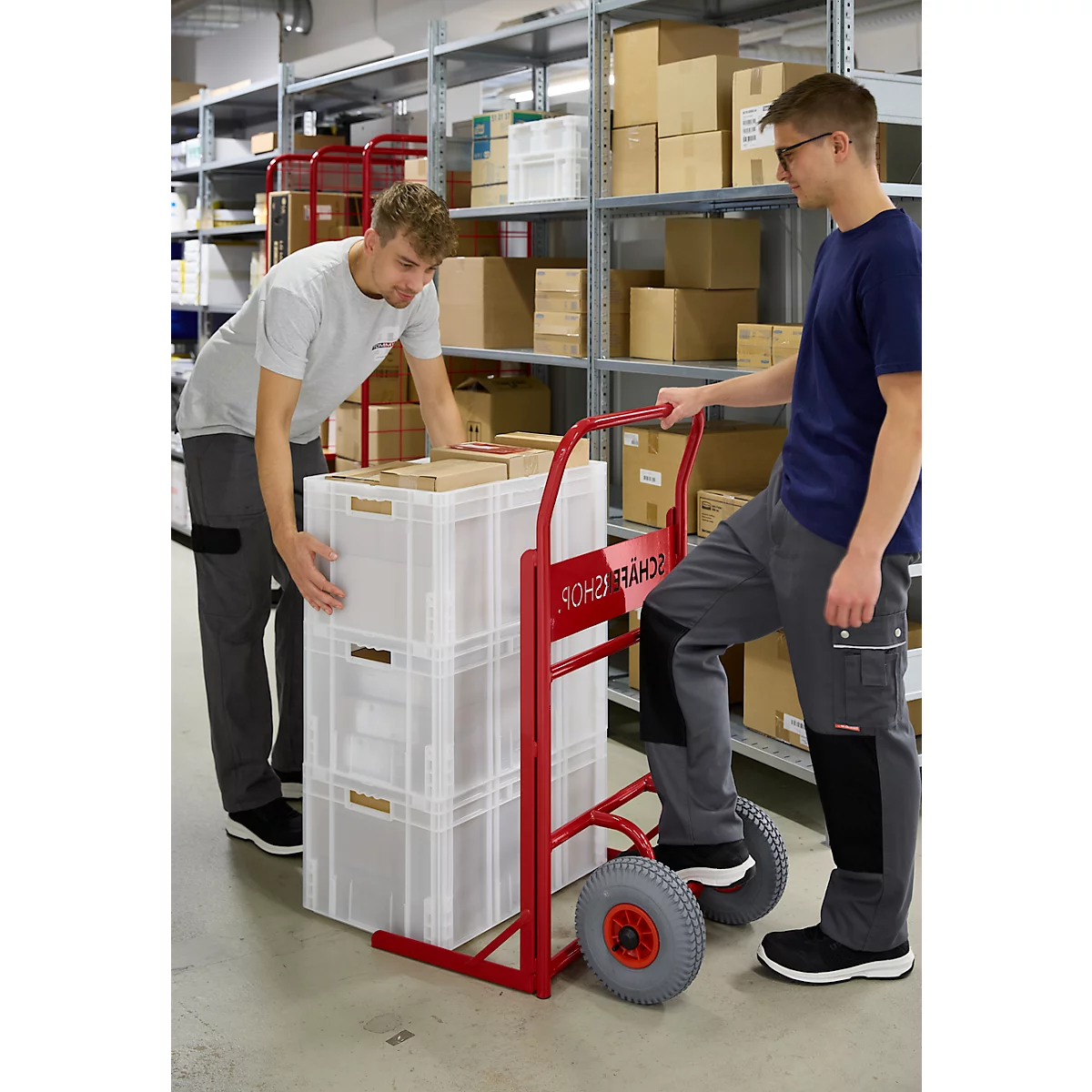 Twee mannen in een magazijn. De een tilt een krat op een rode kar, de ander houdt hem vast.