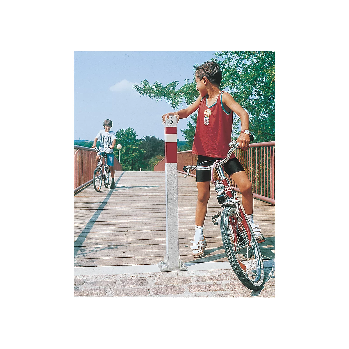 Two boys cycling across a bridge, one holding onto a red and white marker.