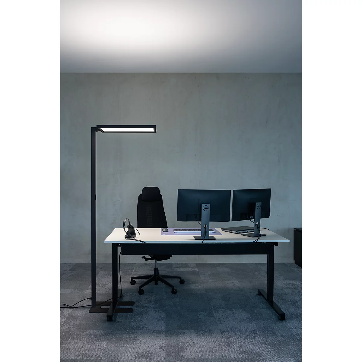 Büro mit Schreibtisch, Monitoren, Stehleuchte und Bürostuhl.