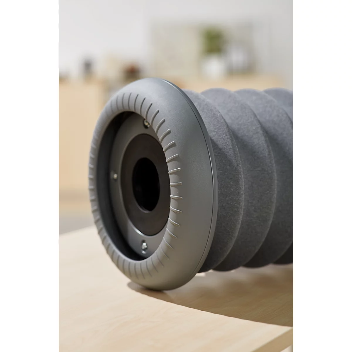 Close-up of a grey fascia roller. The ridged roller lies on a wooden surface.