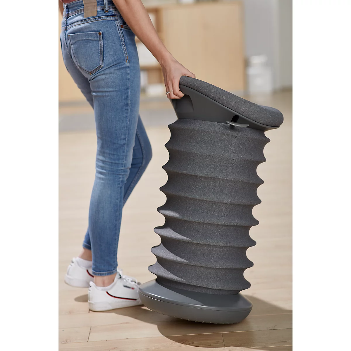 Person holding a gray, spiral-shaped stool. The person is wearing blue jeans and white shoes.