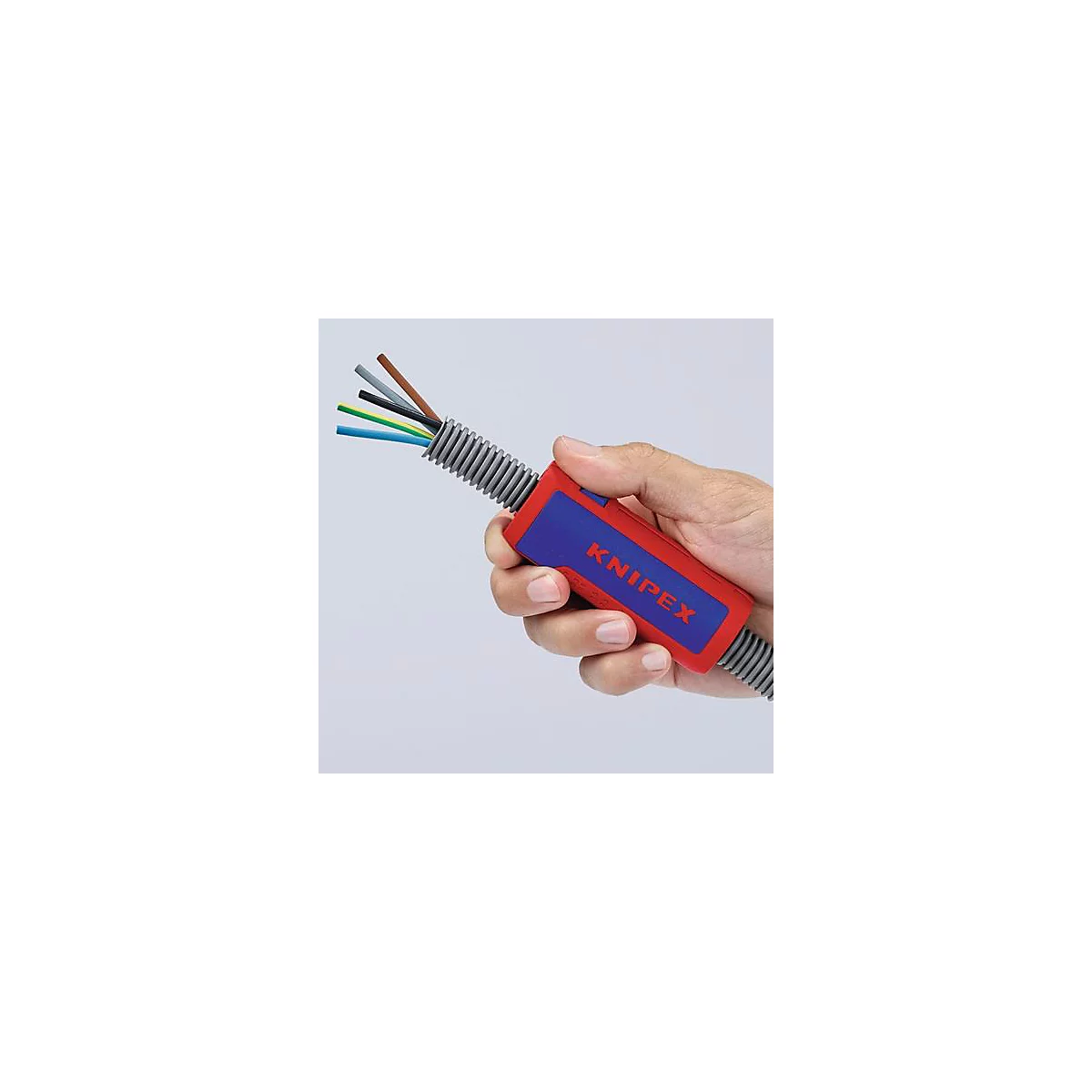 Hand houdt een rood, blauw KNIPEX gereedschap vast. Kabels zitten in een grijze geribbelde buis. Enkele draden steken uit.