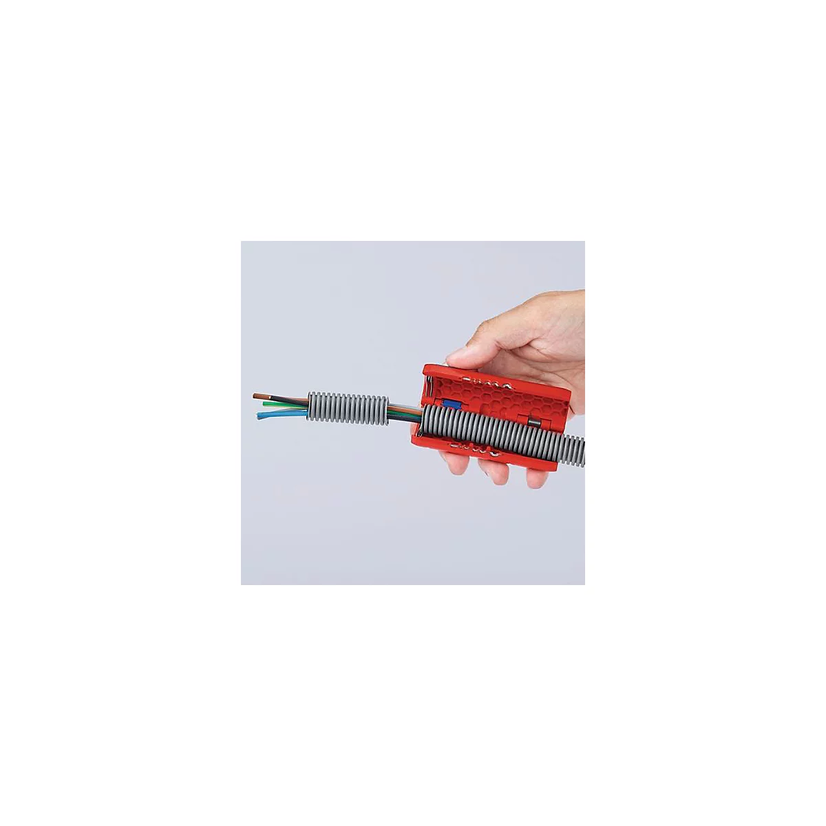 Hand die een rood gereedschap vasthoudt dat een grijze kabelgoot opent met gekleurde kabels die erdoorheen lopen.