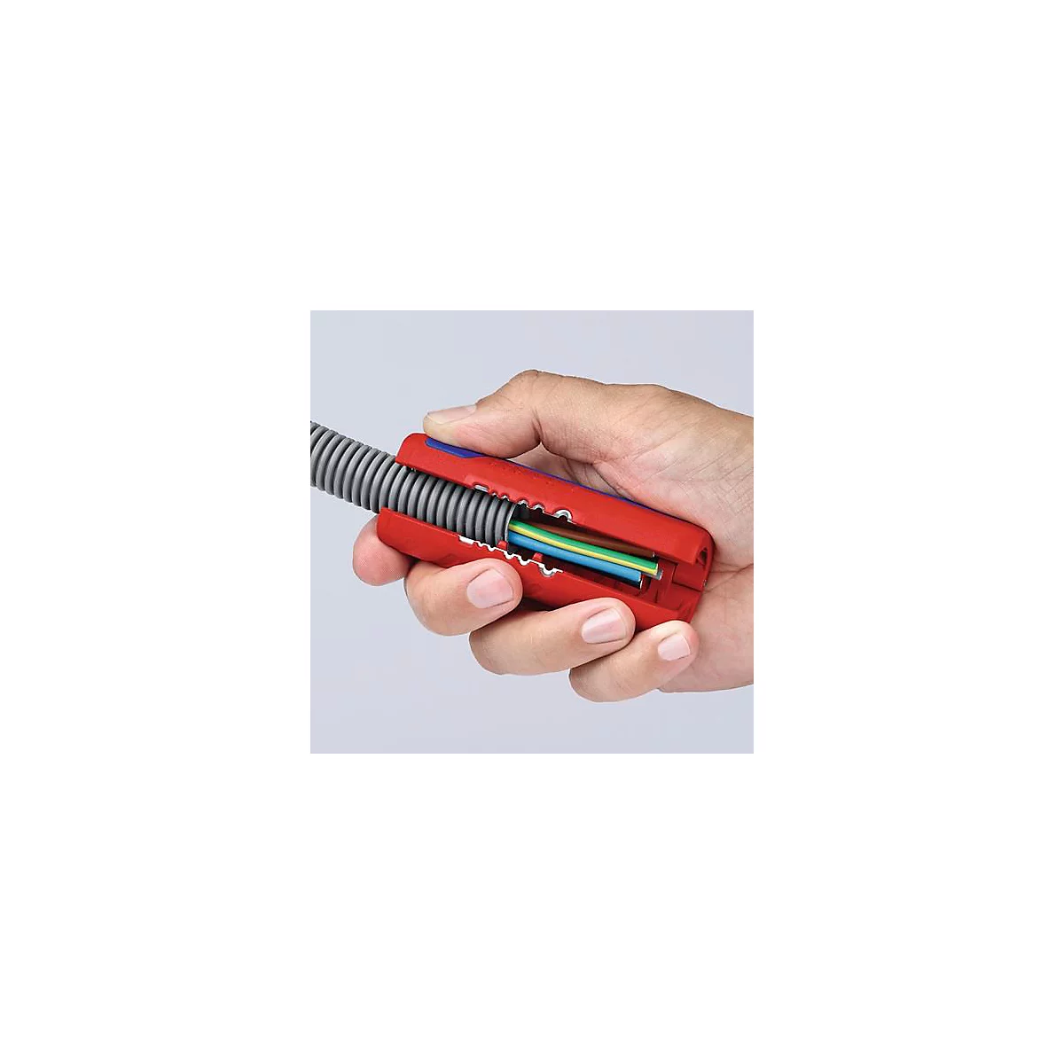 Hand holding a cable stripping tool. Red pliers, gray tube, colored cables visible.