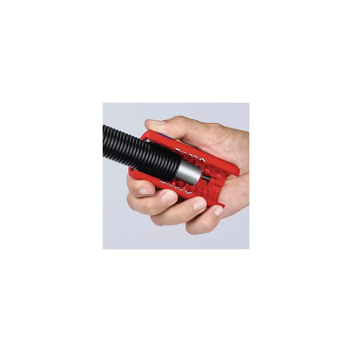 A hand holds a red tool clamping a black, corrugated hose.