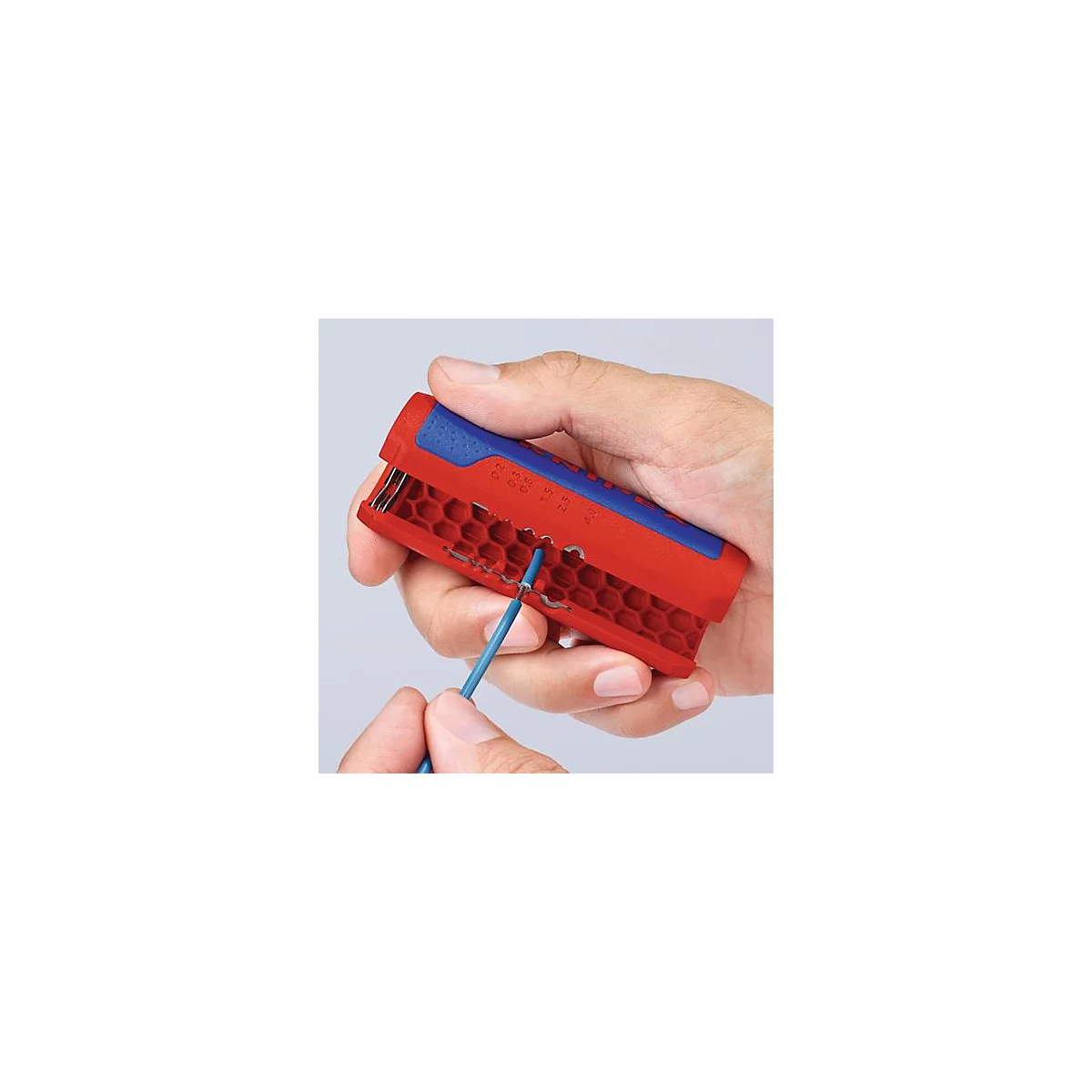A hand holds a red and blue wire stripper. A blue cable is being processed.