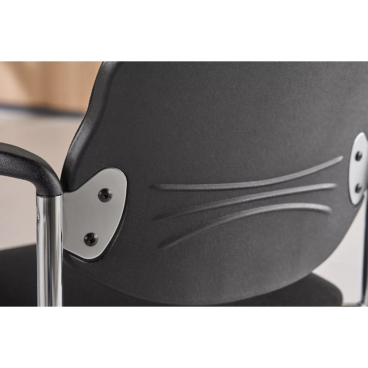Detail of a black chair back with decorative lines and metal connections.