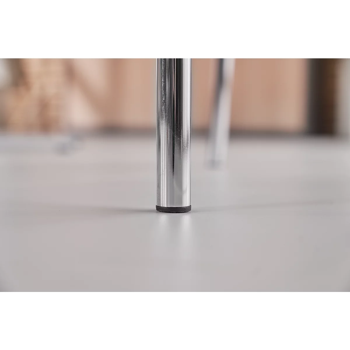 Close-up of two chrome chair legs standing on a light floor. The legs have black plastic feet.