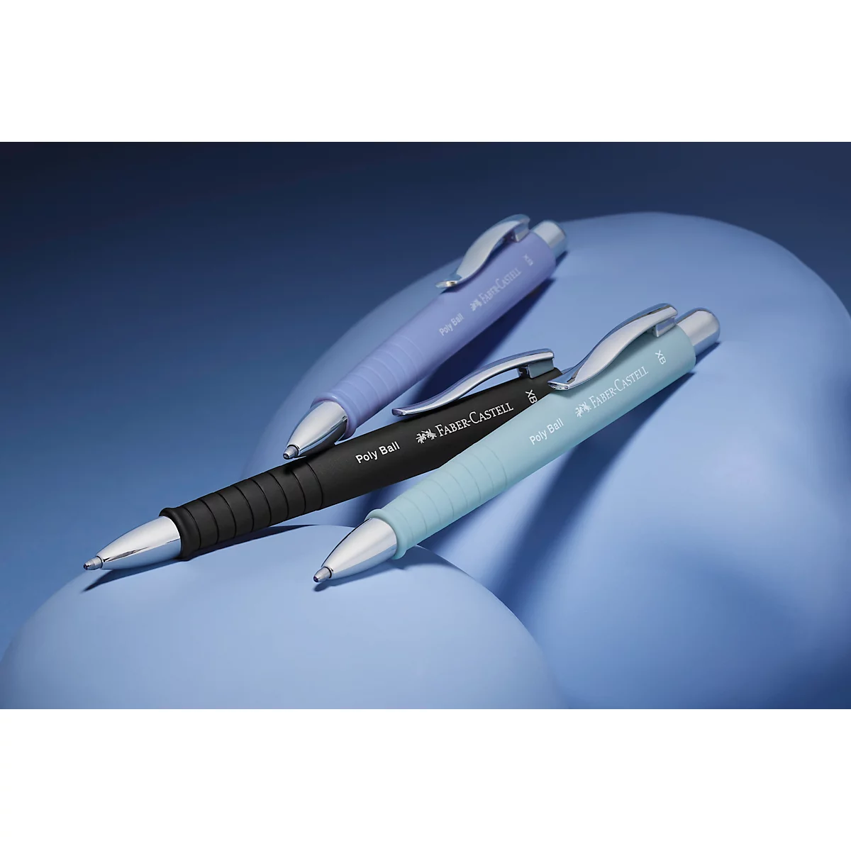 Trois stylos à bille Faber-Castell aux tons pastel sur des formes bleues organiques.