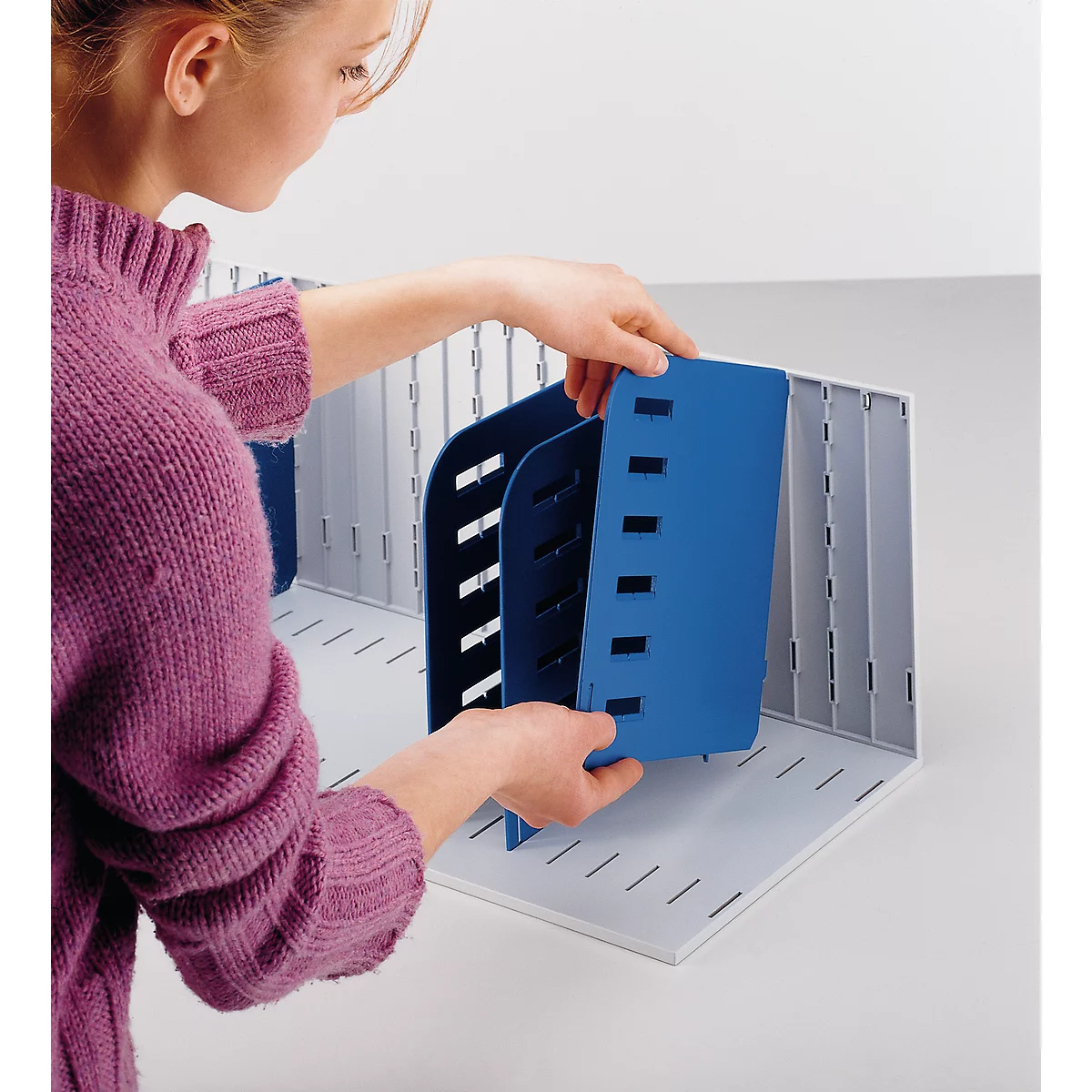 A woman inserts a blue divider into a gray filing system.