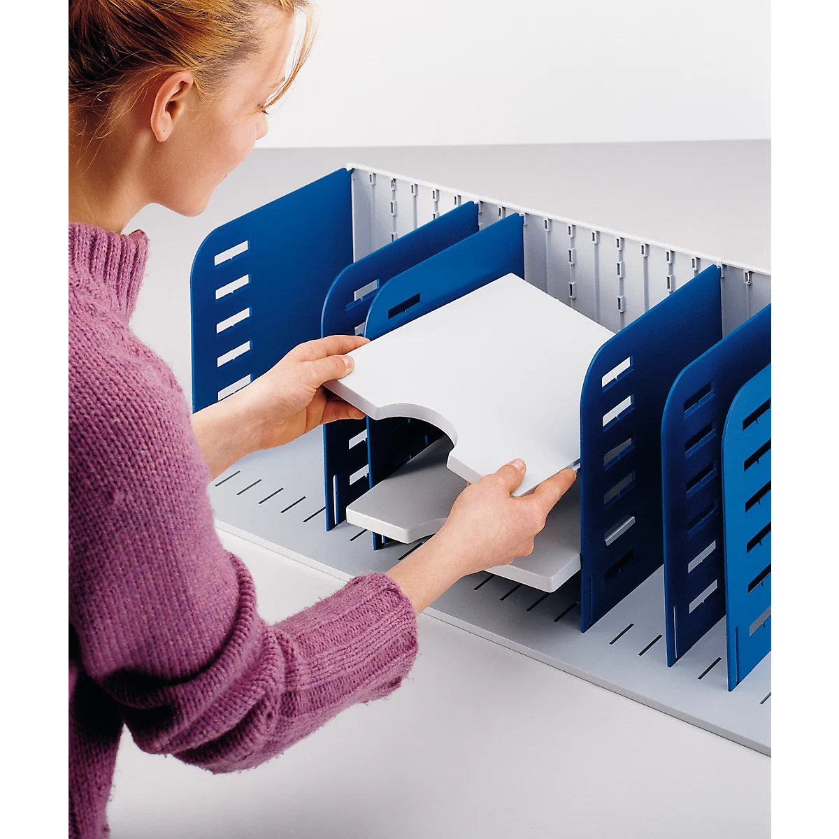 A woman inserts a white shelf part into a blue filing system.