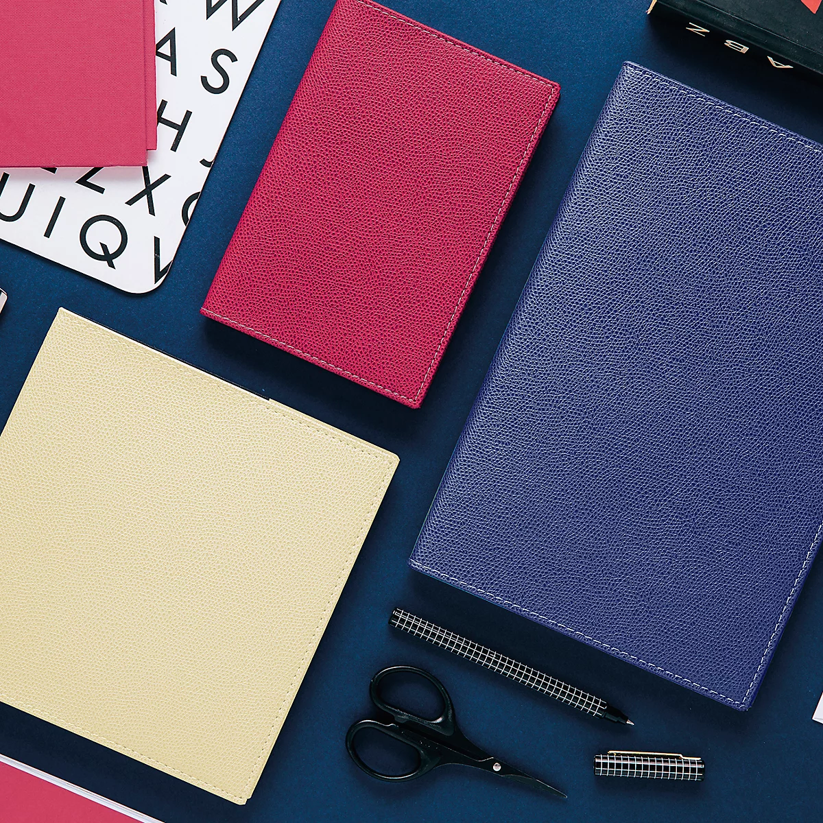 Vue aérienne de cahiers et d'accessoires, en rouge, bleu et crème sur une surface bleue.