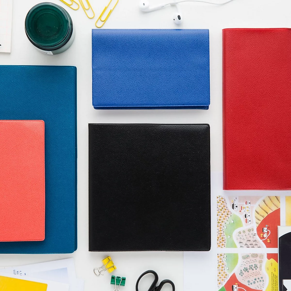 Vue aérienne de divers cahiers en rouge, bleu et noir, entourés de fournitures de bureau.