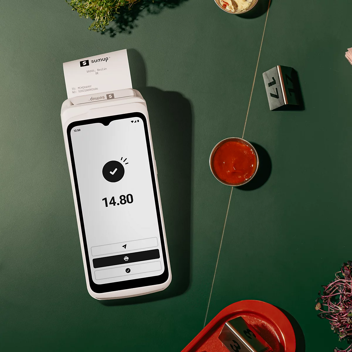 Ein mobiles SumUp-Kartenzahlungsgerät mit Bildschirm, auf dem 14,80 € angezeigt werden. Auf dem Tisch befinden sich auch Saucenschalen.