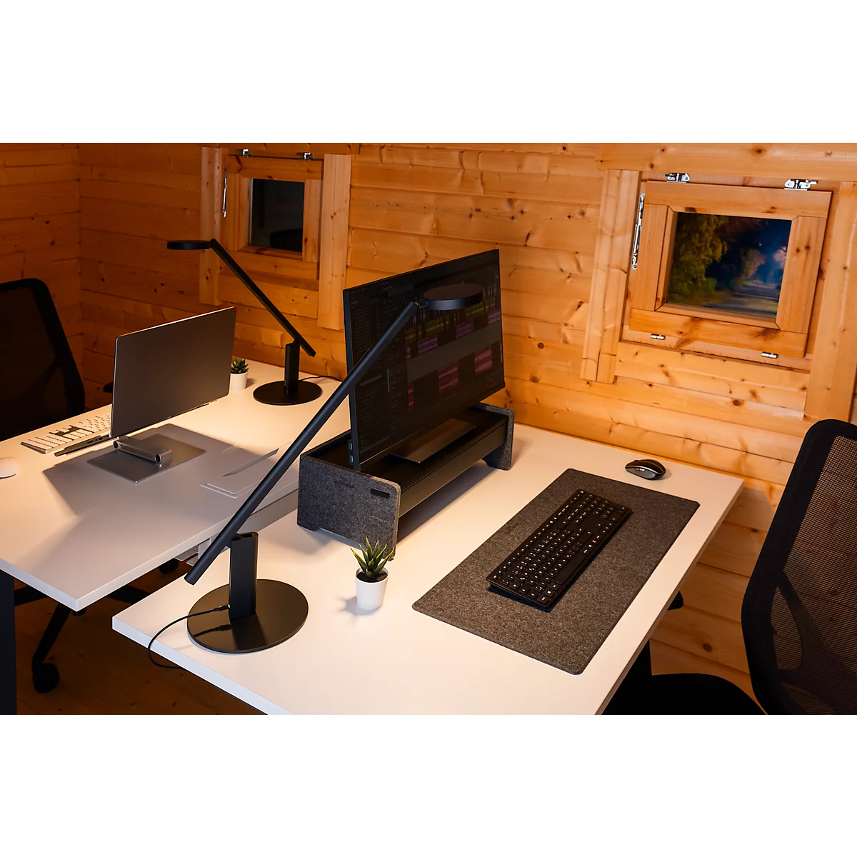 Deux bureaux dans une maison en bois. Sur les tables : moniteurs, claviers, lampes de bureau et ordinateurs portables.