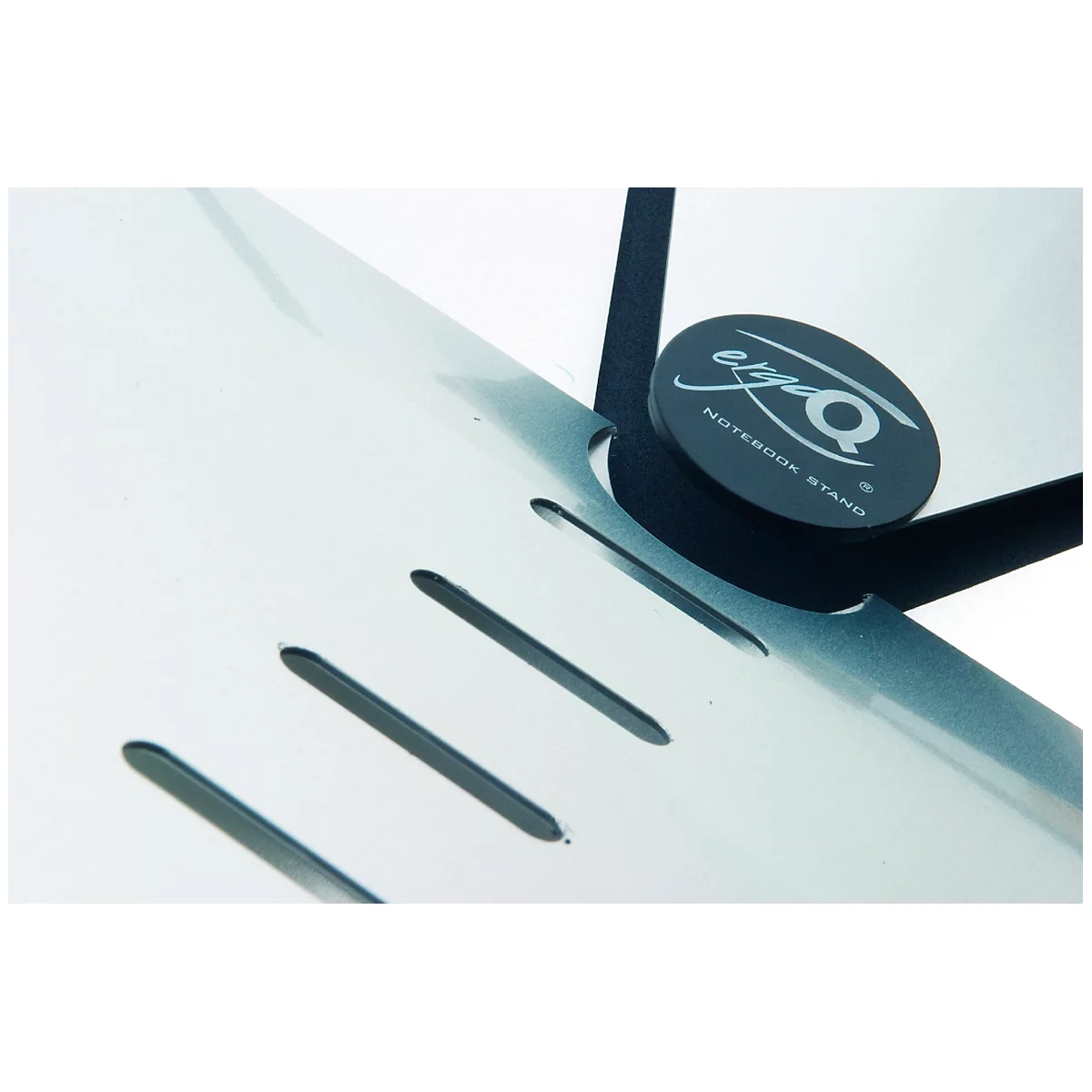 Gros plan d'un support pour ordinateur portable. Le métal blanc perforé rencontre des éléments noirs, un panneau rond avec lettrage.