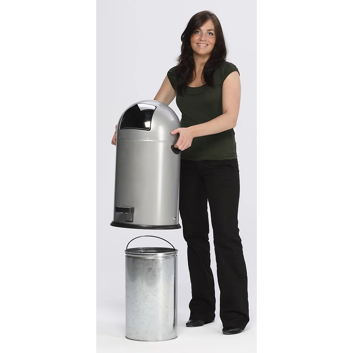 Une femme tient le couvercle d'une poubelle argentée, en dessous se trouve la poubelle cylindrique. Fond neutre.