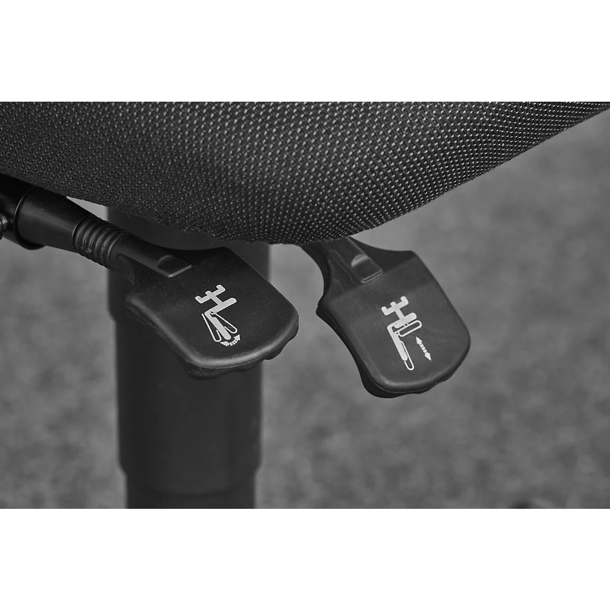 Close-up of two black levers on an office chair, with white symbols. The chair is made of fabric, in grayscale.