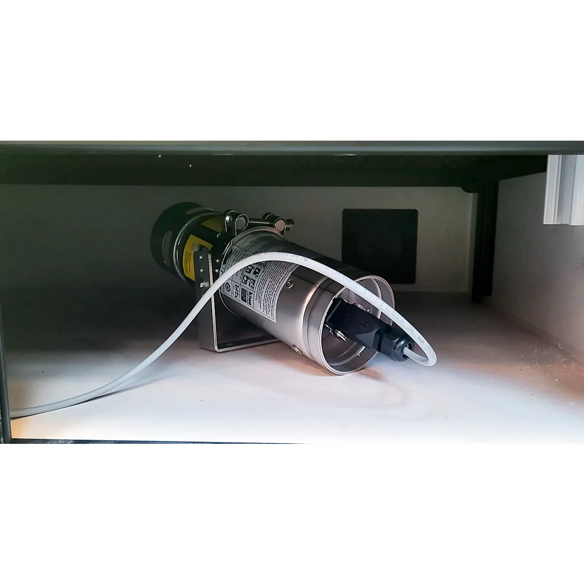 Objet métallique cylindrique avec tubes et support, placé dans un boîtier ombragé.