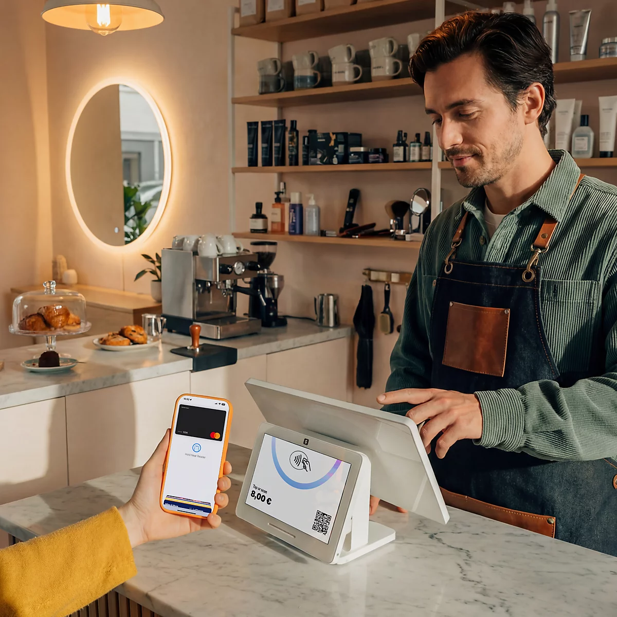 Un barista utilise un terminal de paiement lumineux pendant qu'un client paie sans contact avec un smartphone.