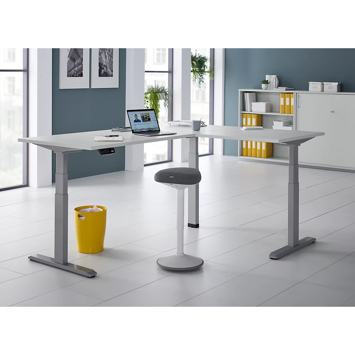 Bureau d'angle avec ordinateur portable, chaise de bureau et poubelle jaune.