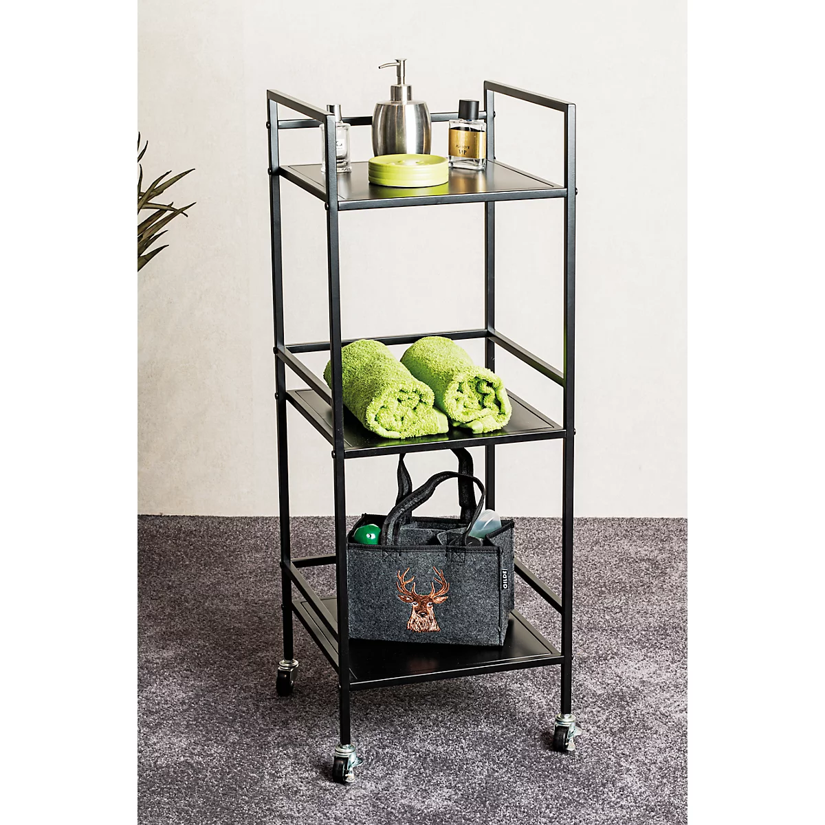 Étagère de salle de bain noire à trois étagères. Serviettes, savon, flacons et un sac avec un motif de cerf sont placés.
