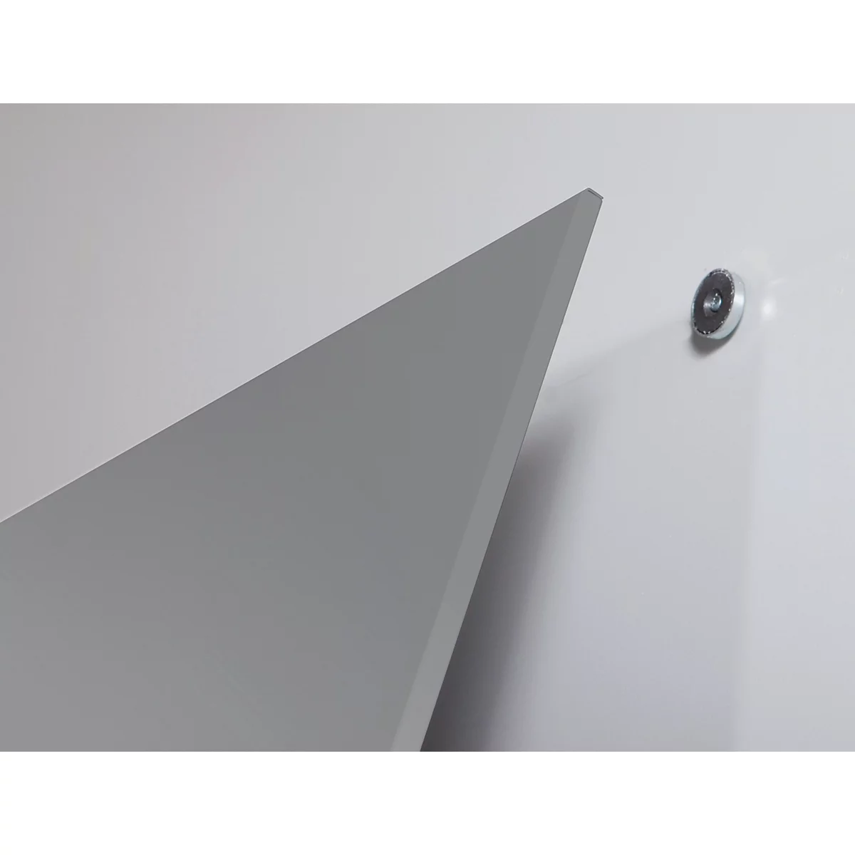 Forme triangulaire grise contre un mur blanc, avec une pièce métallique.