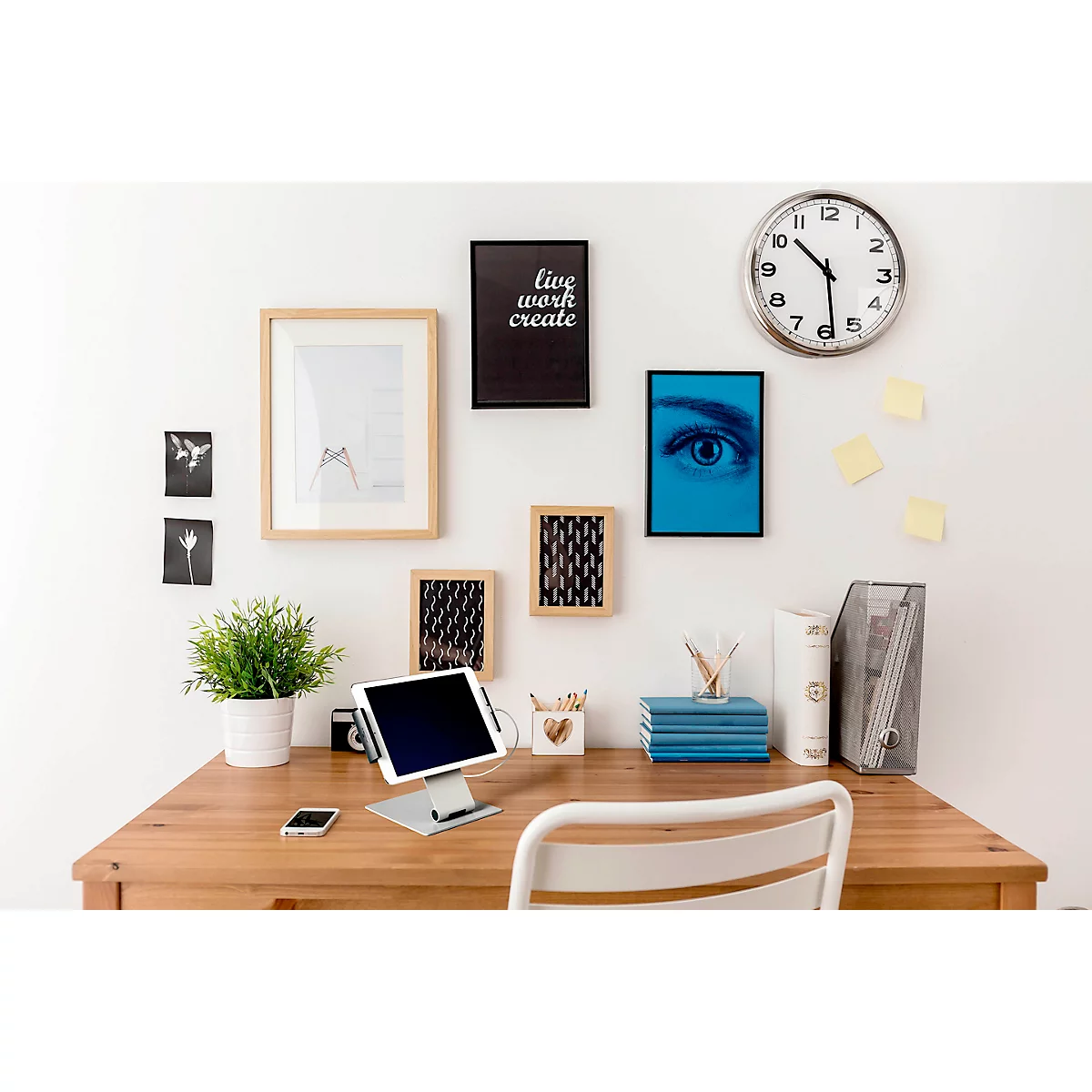 Desk with tablet, plants, pictures and clock. On a black picture says: live work create.