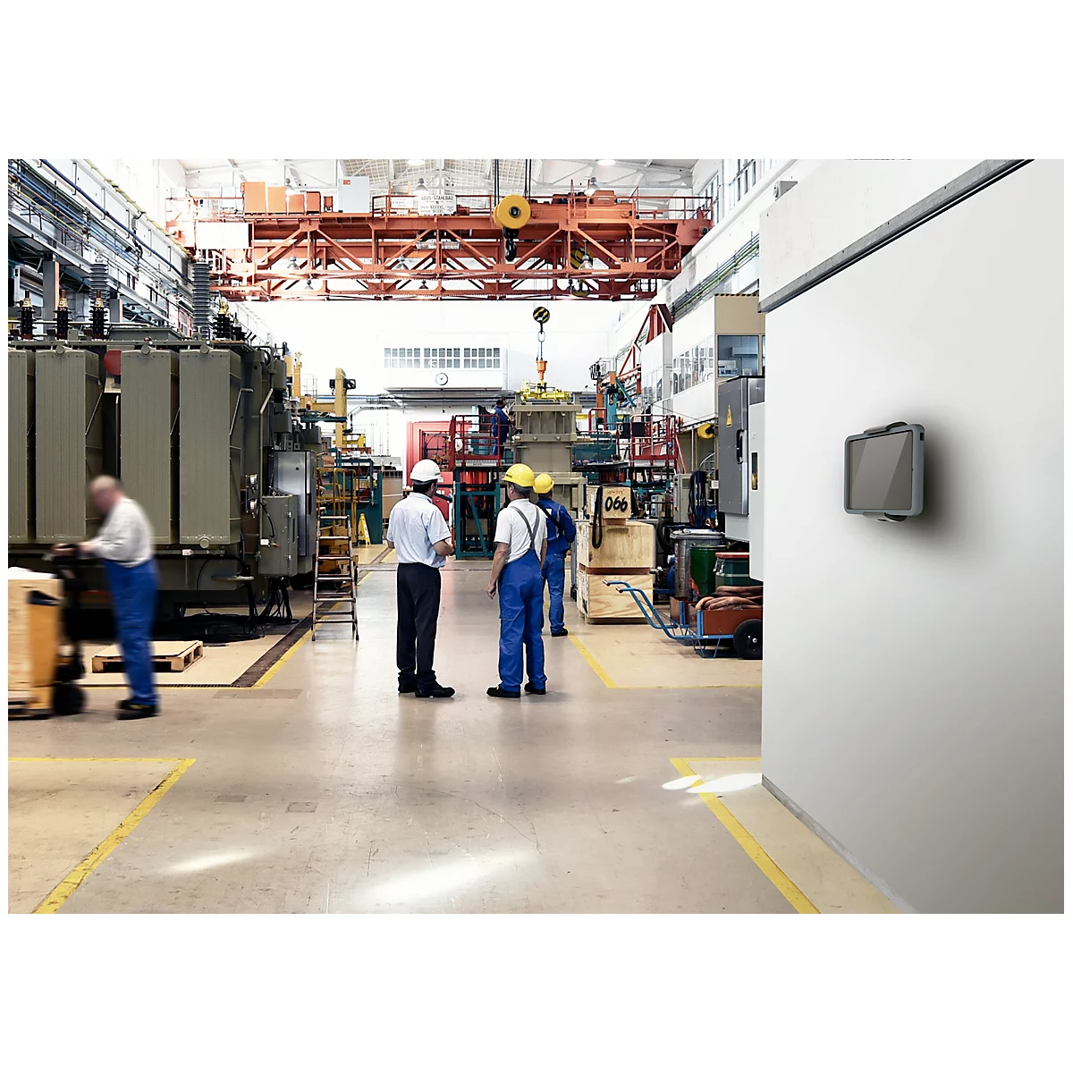 Factory workers working on a machine. A screen on the wall. Yellow markings on the floor.