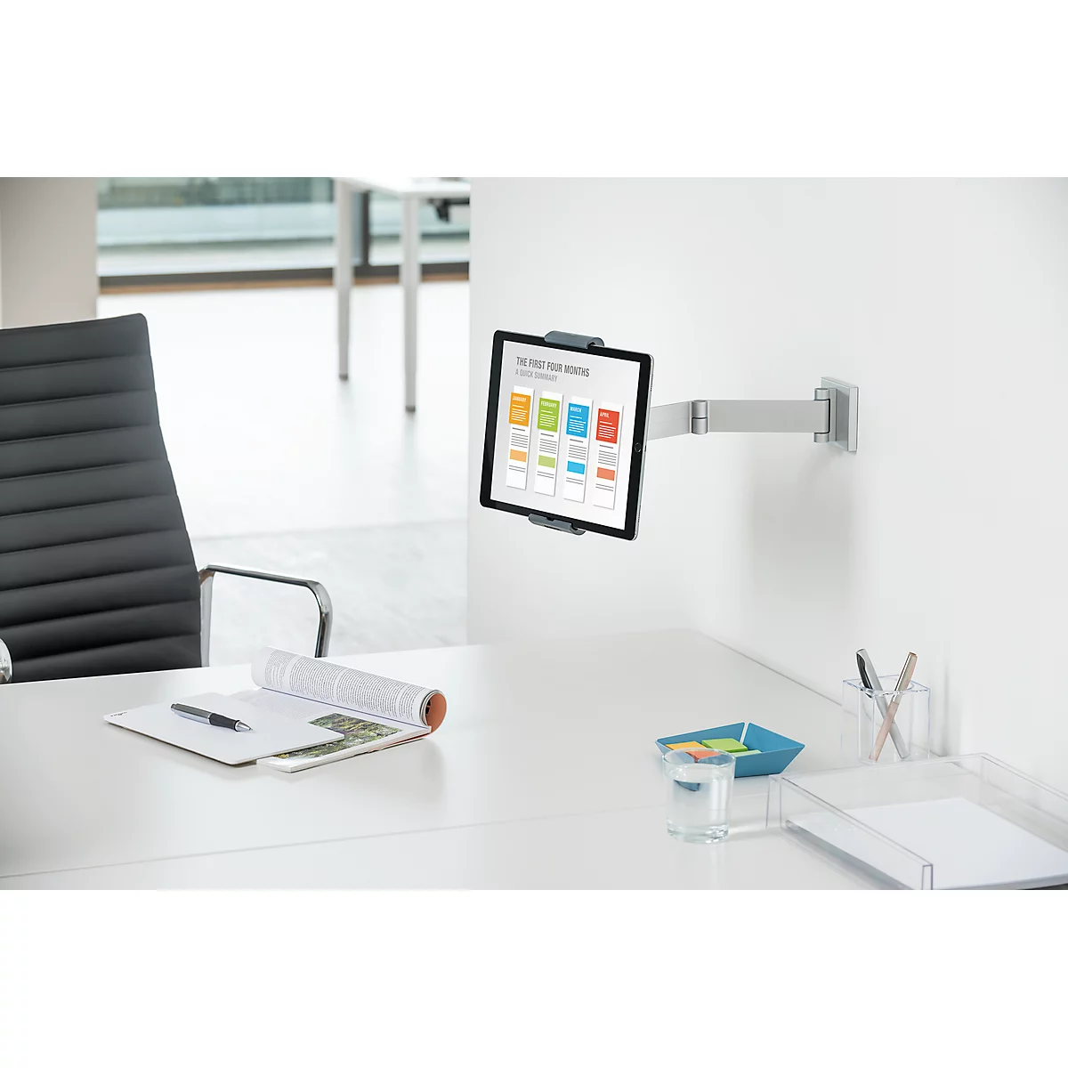 Tablet on wall mount, notes, pens, a blue bowl and a glass of water on the desk.