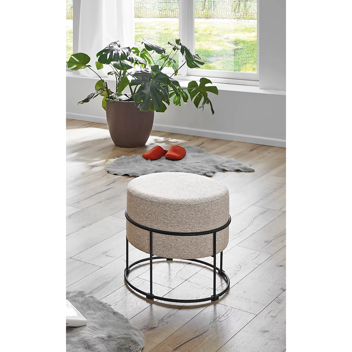 Tabouret rond avec revêtement en tissu beige et structure en métal noir. Une plante et des chaussures rouges en arrière-plan.