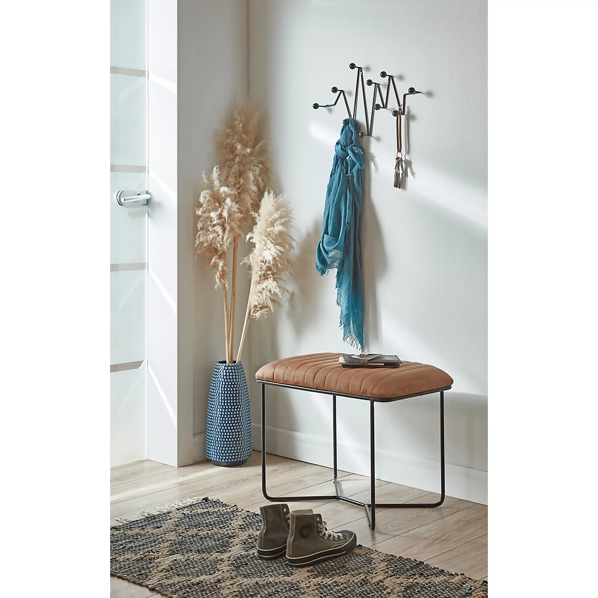 Entrée avec meubles en bois : porte-manteau, miroir, tabouret. Une fenêtre offre une vue sur les arbres et les bâtiments. Ambiance accueillante et lumineuse.