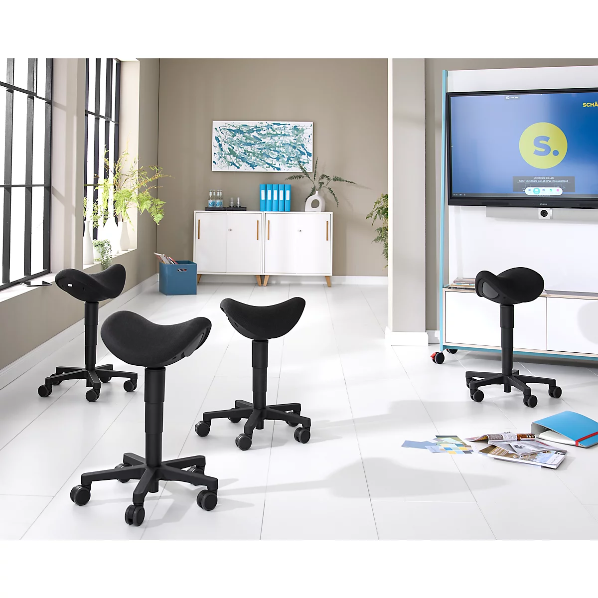 Quatre chaises selle noires dans une pièce lumineuse. En arrière-plan, une armoire, une télévision et une œuvre d'art.