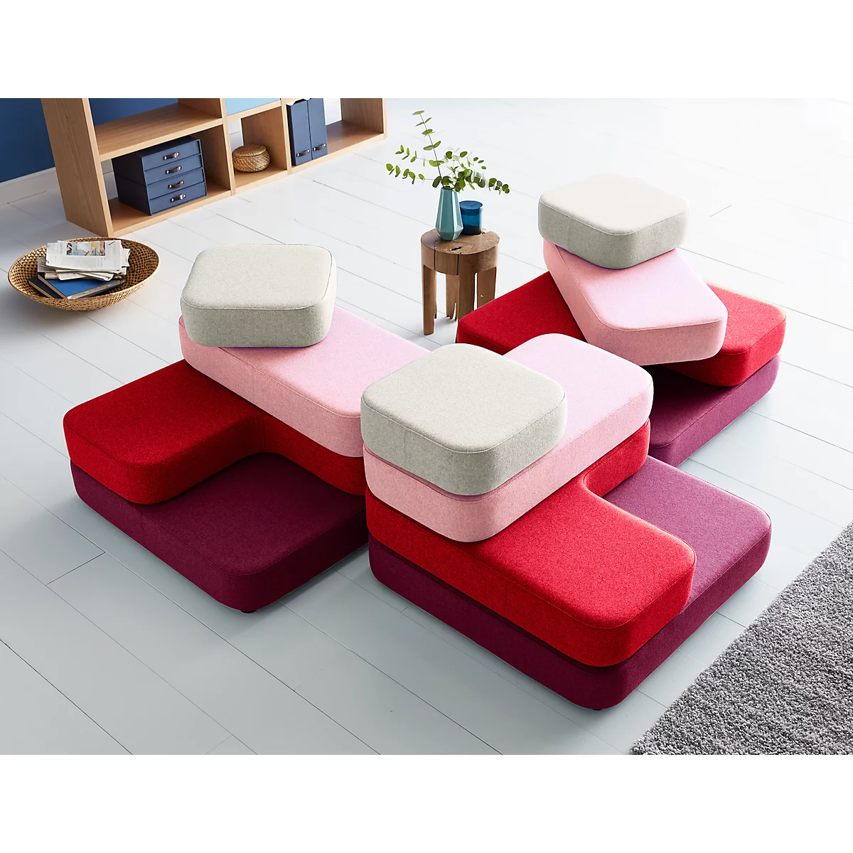 Multi-colored, modular sofa pieces; red, pink, and beige. On a white floor and gray carpet.