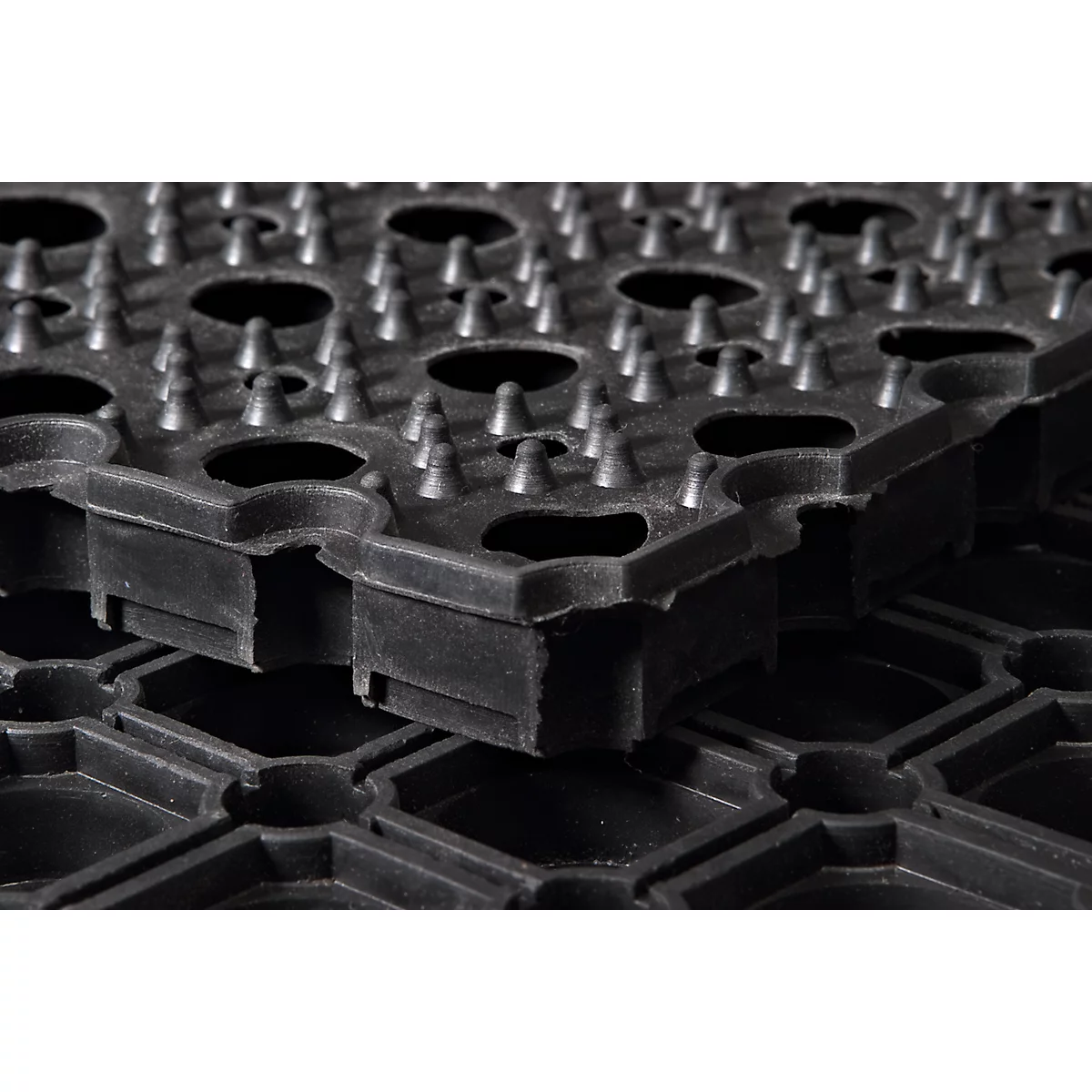 Gros plan d'un tapis en caoutchouc noir avec des clous et des ouvertures hexagonales. Deux tapis sont empilés.