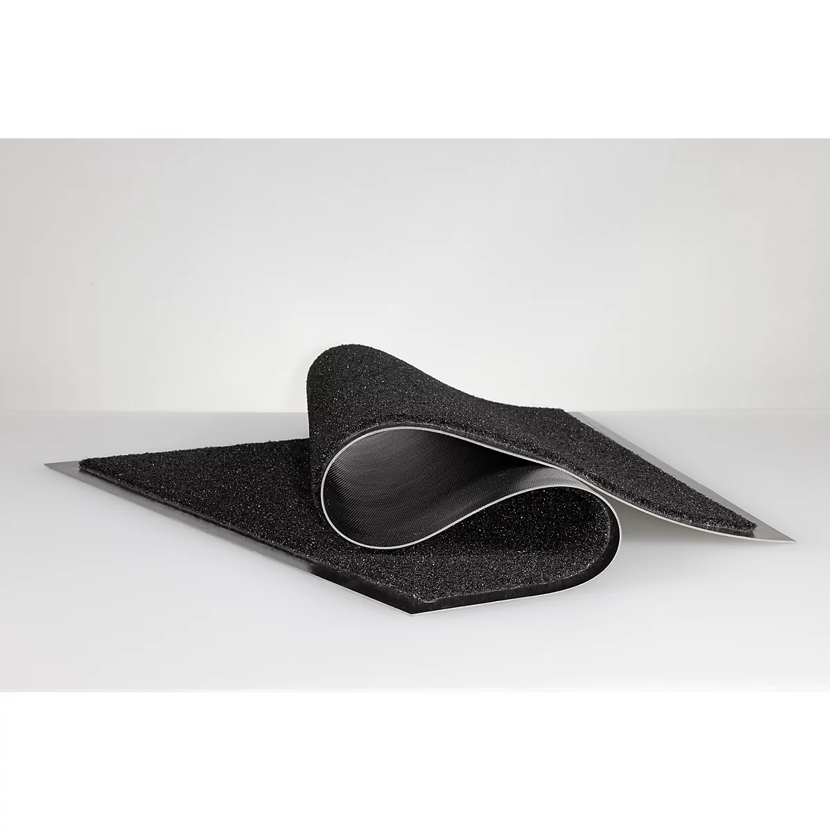 Un paillasson noir et flexible à surface texturée est posé plié sur un fond blanc.