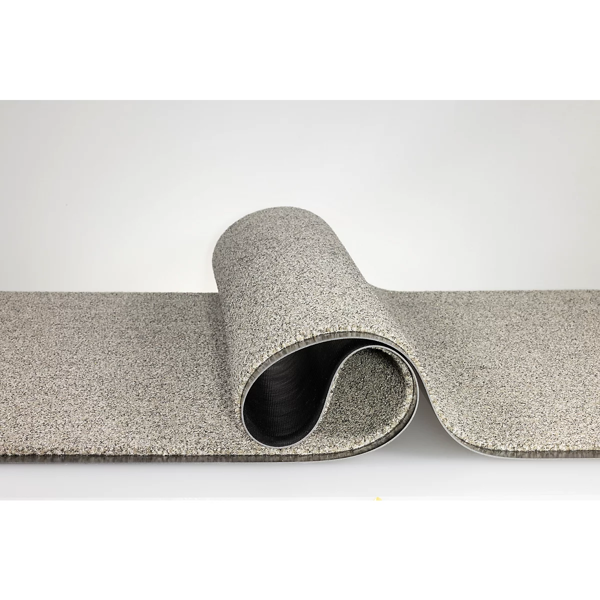 Un revêtement de sol en moquette gris moucheté, enroulé sur un côté pour révéler le dessous noir.